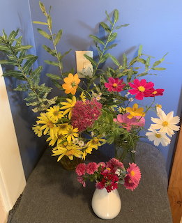 Colorful flower bouquet with daisies and cosmos in white vase on table against blue wall