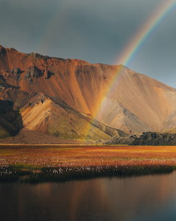 Rainbow over a sunlit mountain and calm lake
