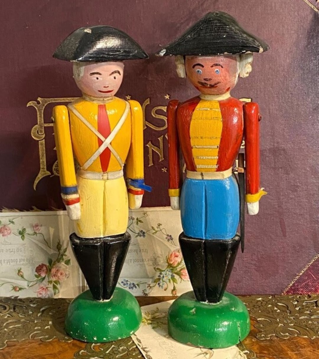 Two vintage hand-painted wooden toy soldier figurines in yellow and red uniforms on green bases
