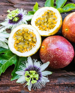 Halved passion fruits showing yellow pulp, whole fruits, passion flower, and green leaves on wood