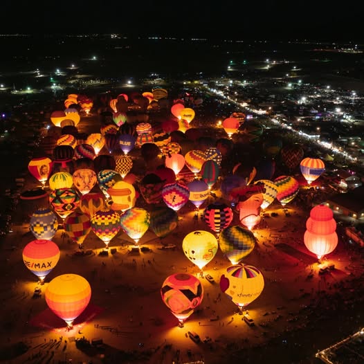 Aerial night view of many illuminated hot air balloons glowing on a festival field