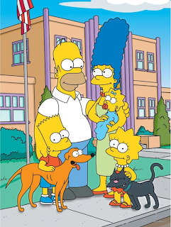 The Simpson family of five with their pets standing in front of their beige house under blue sky