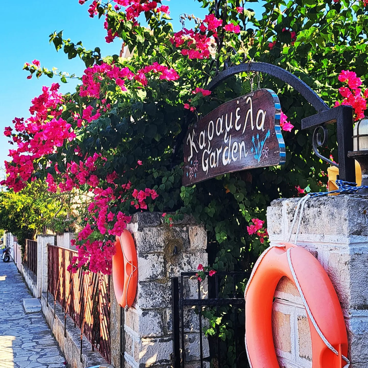 Stone garden gate covered in pink bougainvillea with orange lifebuoys and a hanging sign