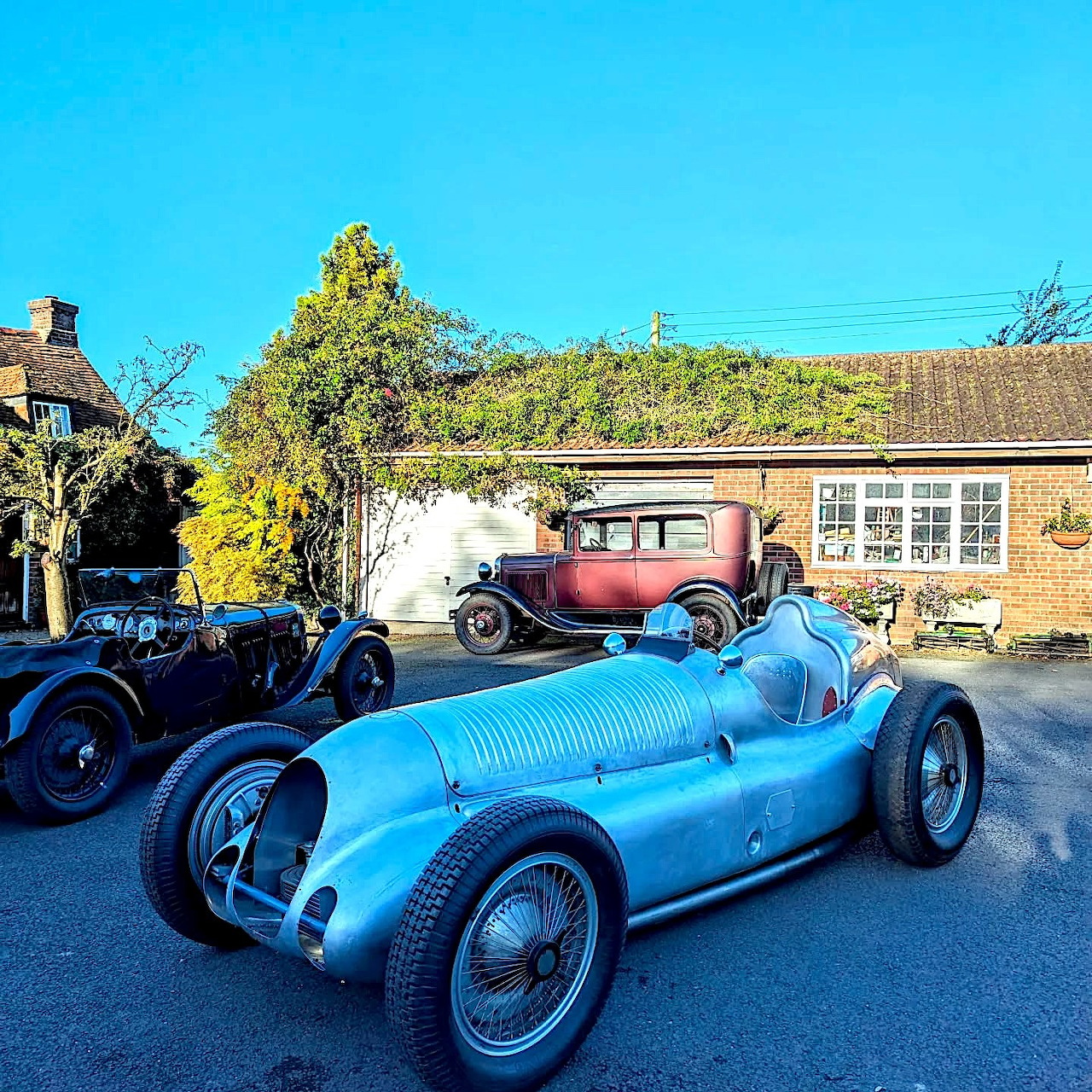 Blue vintage Grand Prix race car parked outdoors with other classic cars near brick buildings