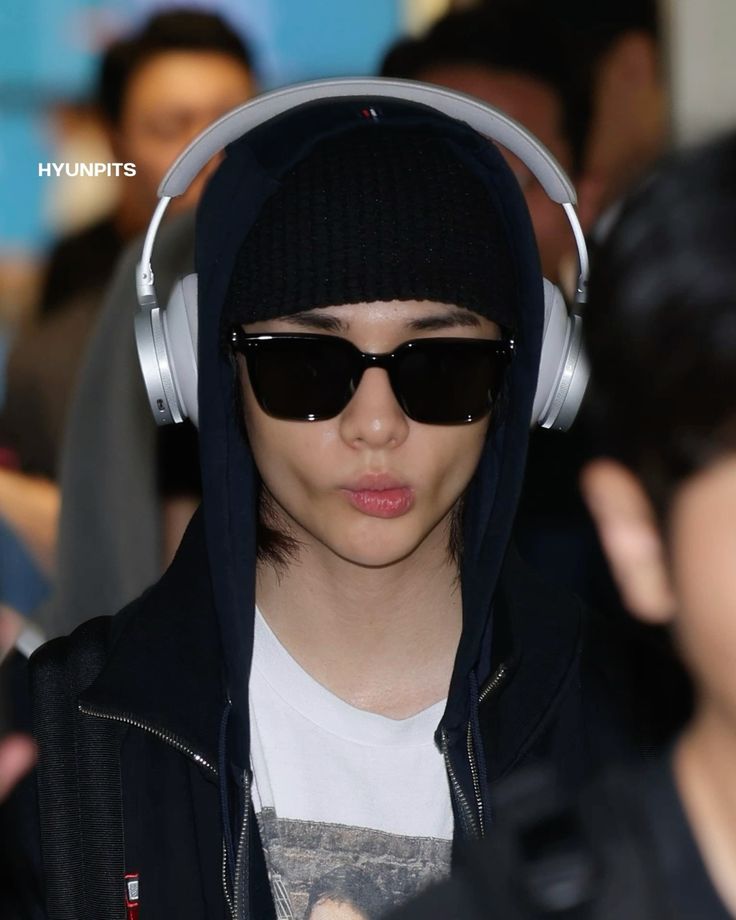 Young man wearing black cap, sunglasses, white headphones and black hoodie in crowd