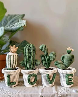 Four amigurumi crocheted cacti in white pots with green letters spelling LOVE on a table