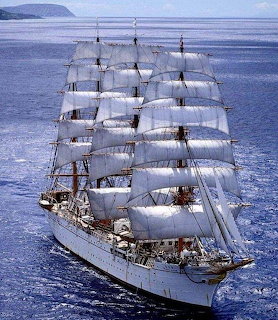 Tall sailing ship with white sails fully deployed on blue ocean