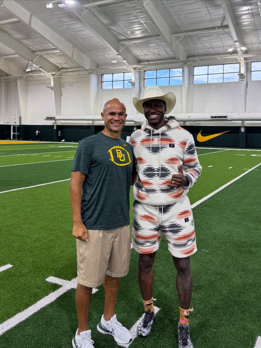 Two men standing together on an indoor football field with artificial turf