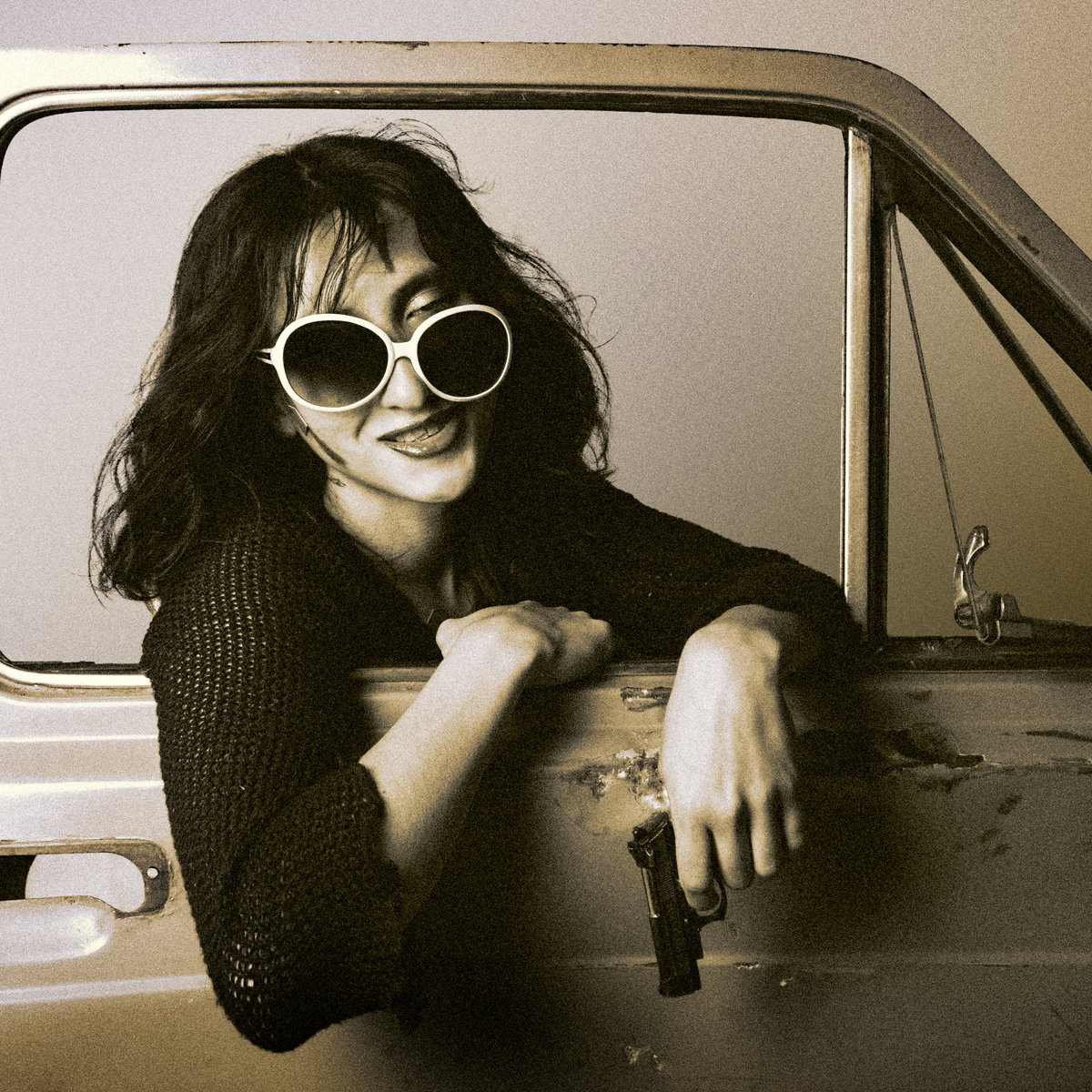 Sepia portrait of a woman in round sunglasses leaning out of a car window