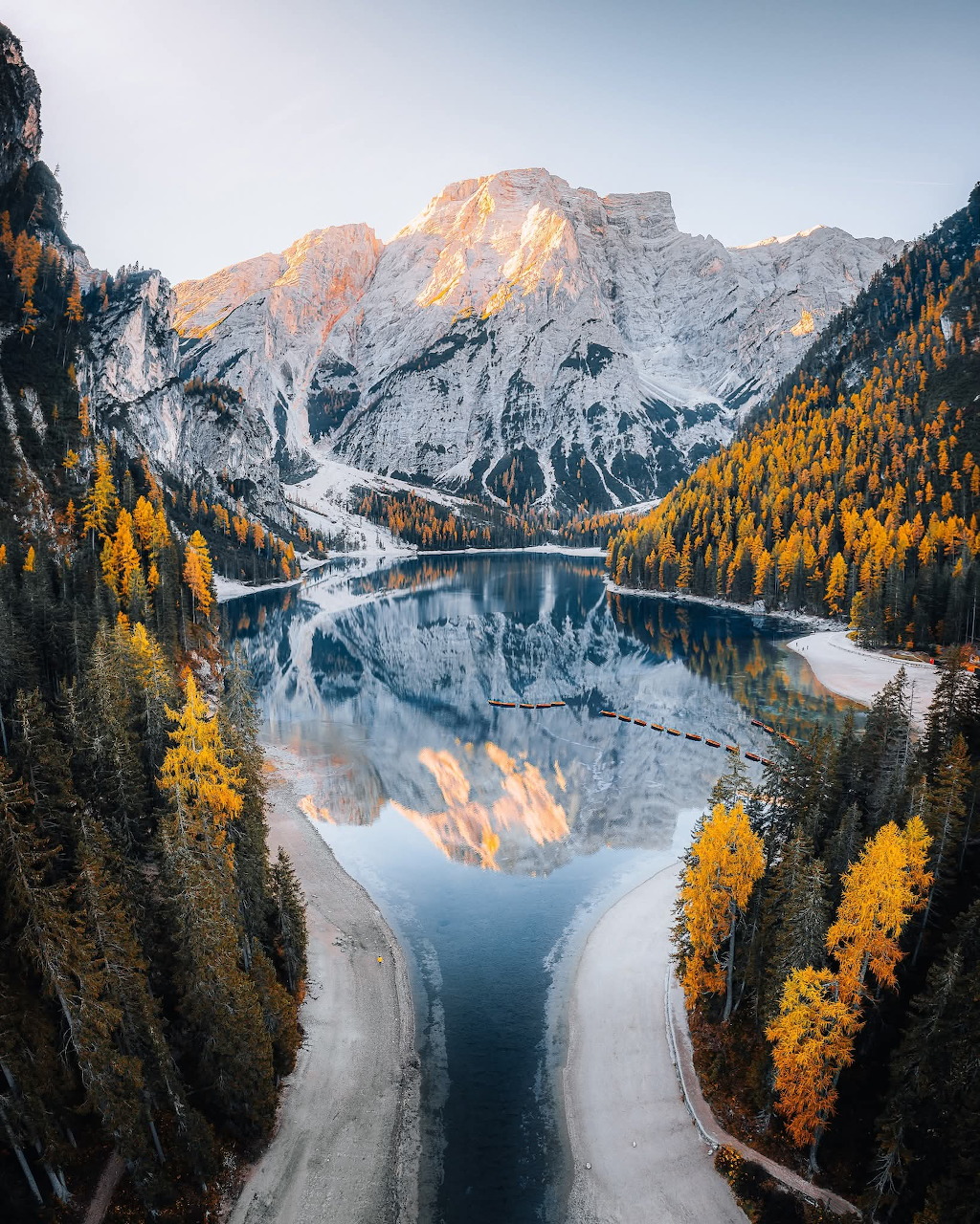 Snowy Dolomites mountains reflected in a calm lake with golden autumn trees