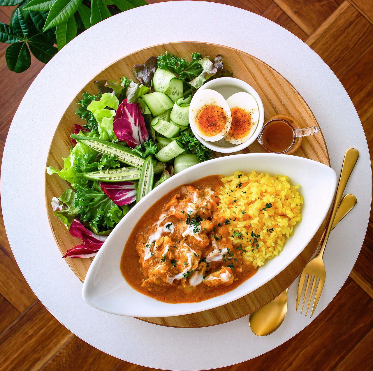 Meal plate with curry, rice, salad, and boiled egg on wooden table