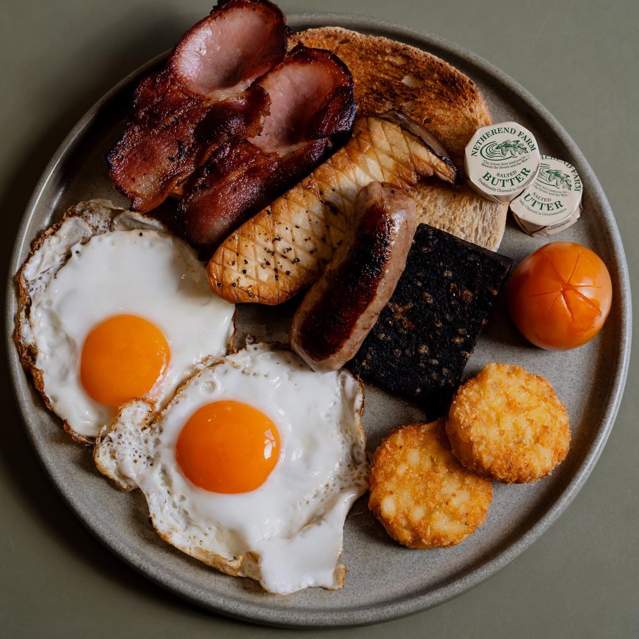 Full English breakfast with eggs, bacon, sausage, toast, hash browns, black pudding and grilled tomato