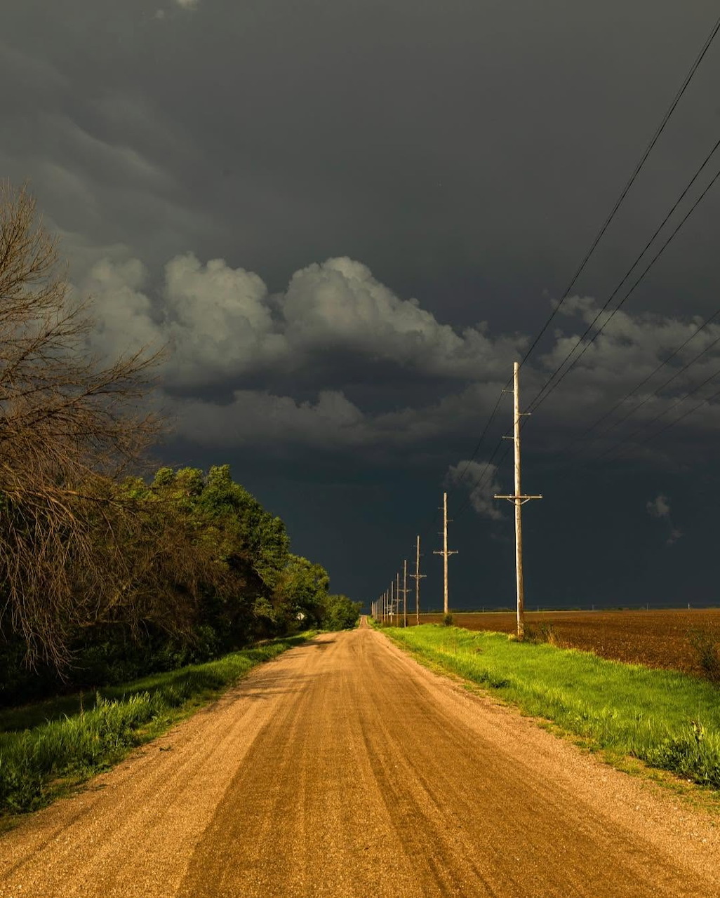 Straight dirt road leading to the horizon under dark storm clouds with power lines alongside