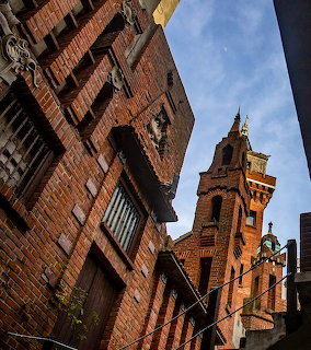 Old brick buildings and a cathedral tower viewed from below against a blue sky