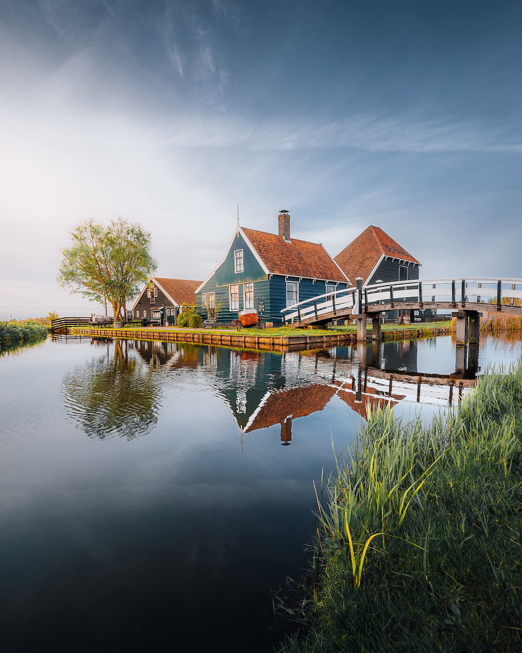Traditional Dutch houses reflected in a calm canal with grass and trees under a blue sky