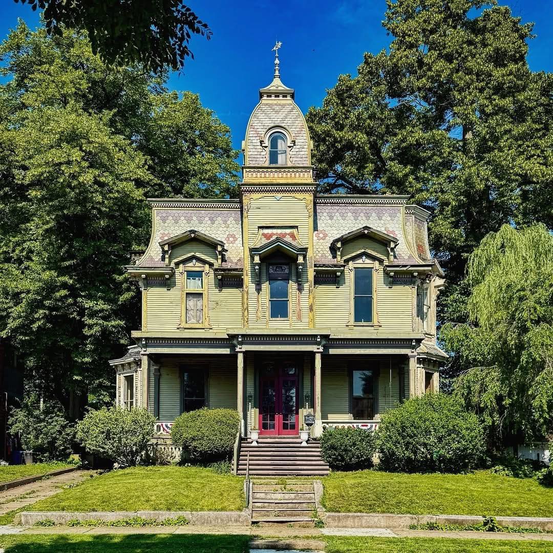 Yellow Victorian house with tower and arched windows surrounded by trees