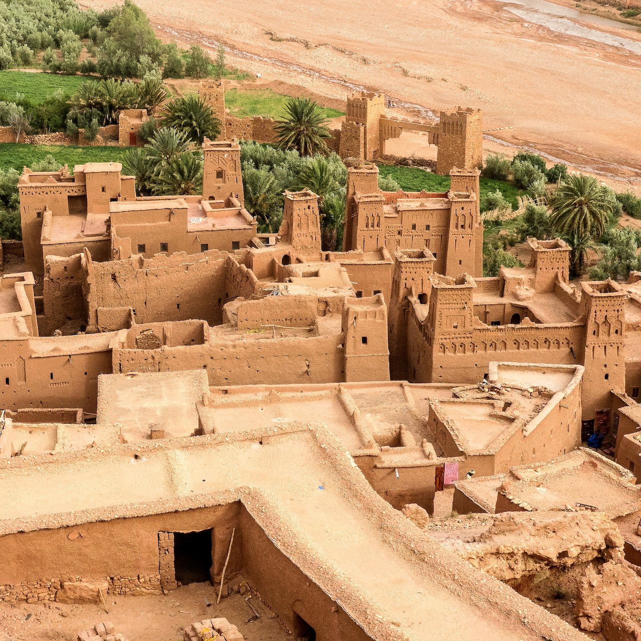 Aerial view of traditional Moroccan kasbah with earthen buildings and palm trees in desert setting