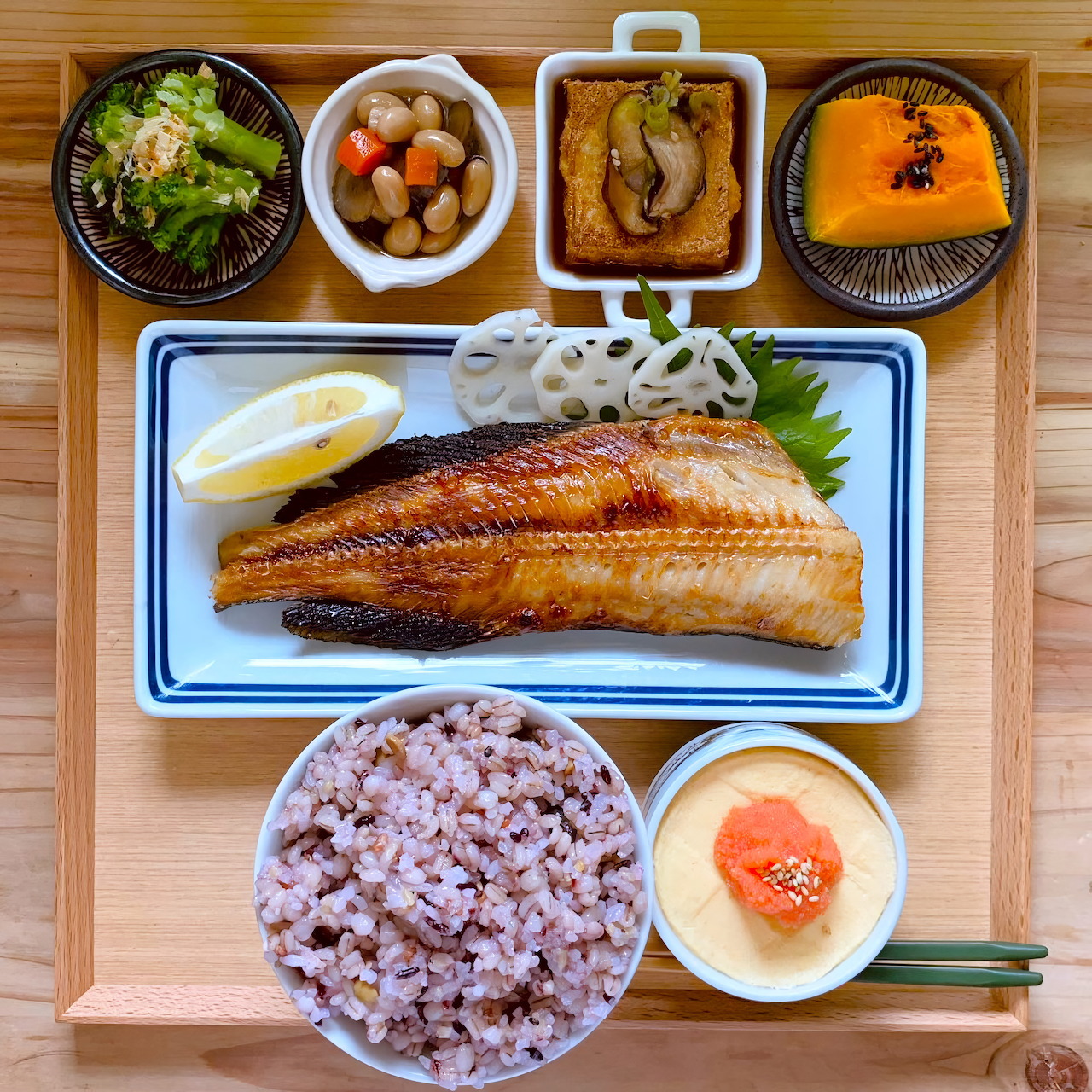 Overhead view of Japanese breakfast with grilled fish, rice, egg, and small side dishes on wooden tray