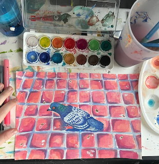 Overhead view of watercolor painting with pink grid pattern on artist's desk with paints and brushes