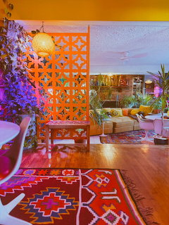 Colorful retro living room with orange lattice divider, kilim rugs, plants, and warm ambient lighting