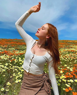 Red-haired woman in white top posing with raised arm in a colorful wildflower field