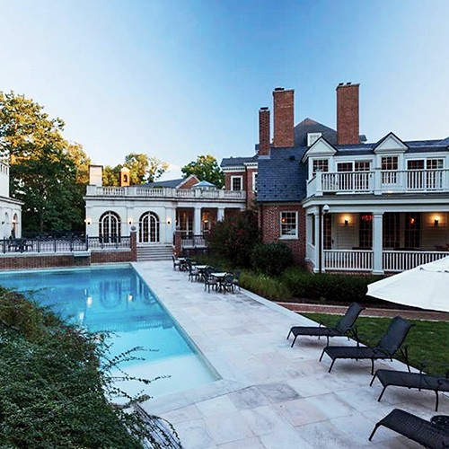 Brick mansion with white columns and balcony beside a rectangular pool at twilight