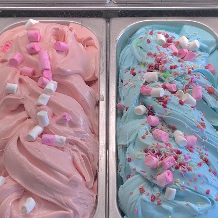 Two gelato trays with pink and blue ice cream topped with marshmallows and sprinkles