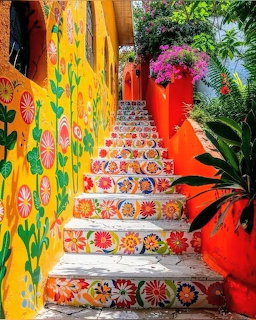Colorful outdoor stairs with decorative floral tiles, bright yellow and orange walls, and tropical greenery