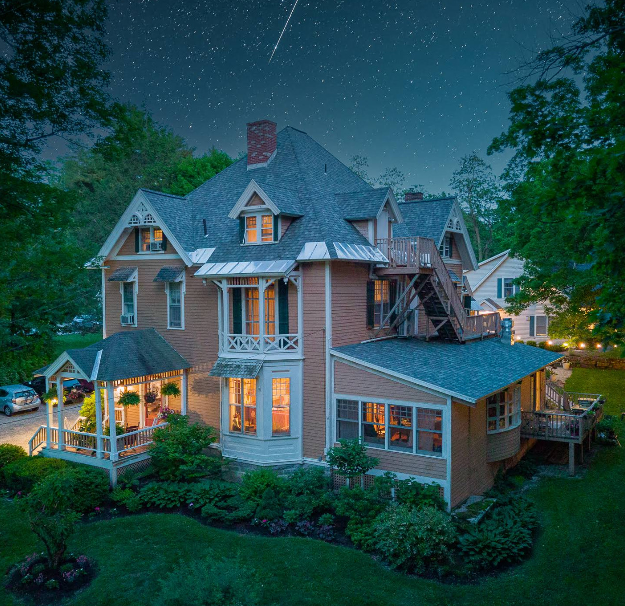 Victorian inn lit up at night with glowing windows surrounded by trees and garden under starry sky