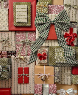 Stacked wrapped gift boxes with patterned paper, bows, and ribbons in red, green, gold, and silver
