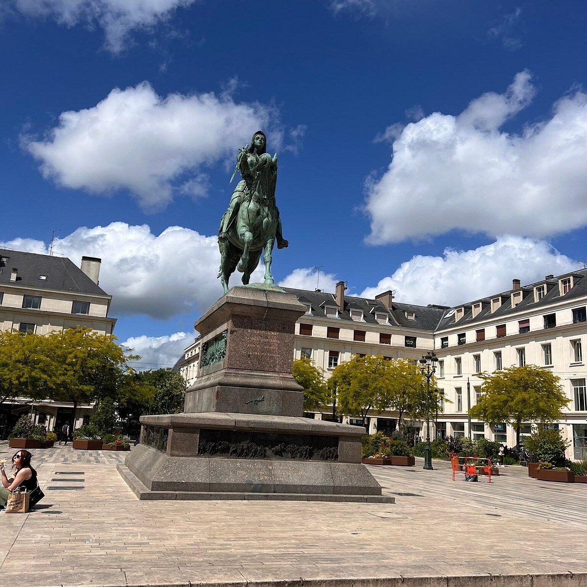Bronze equestrian statue of Johanna von Orléans in a European city square under blue sky with white clouds