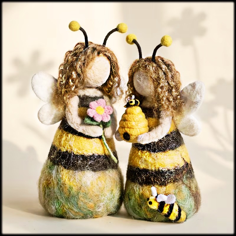 Two handmade felt fairy dolls with bee stripes, wings, and curly hair holding flowers