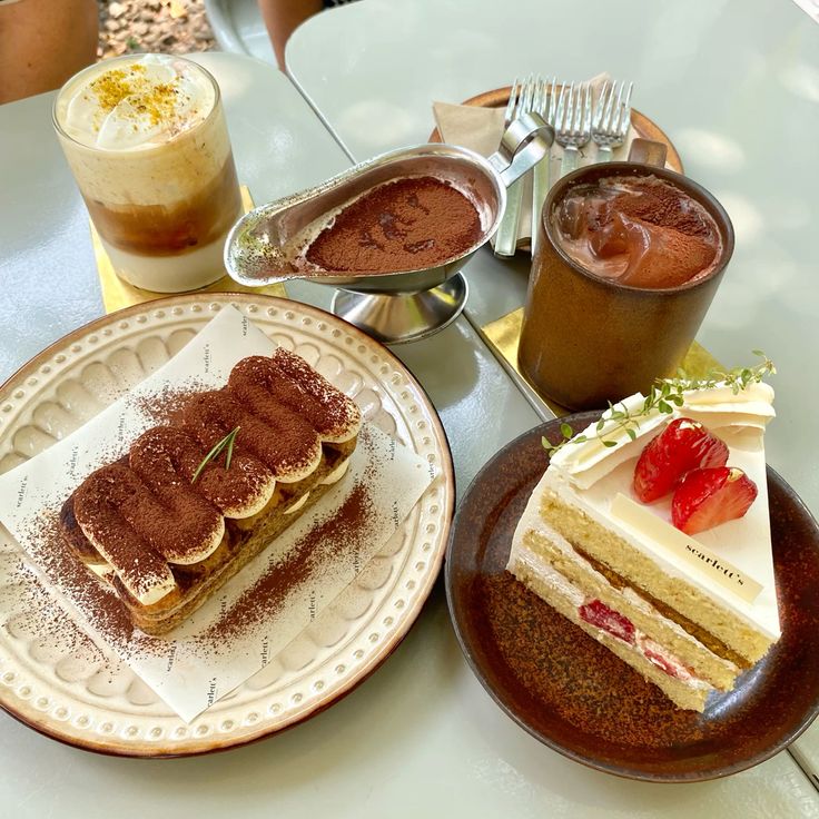 Cafe table with two cake slices, iced coffee, latte, and a small dish of cocoa powder