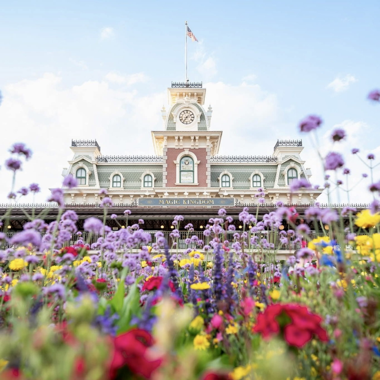 Disney train station with ornate architecture behind colorful flower garden with purple, red and yellow blooms