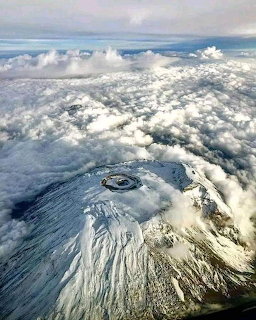 Aerial view of Mount Kilimanjaro's snow-covered volcanic crater above clouds
