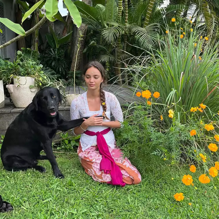 Woman in floral dress sitting with black dog in garden with orange flowers