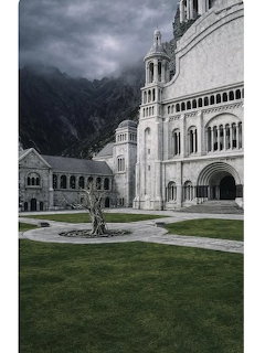 Gothic cathedral with arched windows and towers against dark mountains and overcast sky