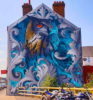 Large colorful owl mural with swirling blue and white patterns painted on brick building gable end