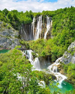 Cascading waterfalls flowing through rocky cliffs surrounded by green forest into turquoise pools