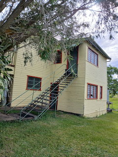 Two-story cream weatherboard farmhouse with red trim and external metal staircase under eucalyptus trees