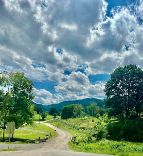 Winding country road through green valley with mountains and dramatic cloudy sky