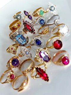 Collection of many gold and silver rings with colorful gemstones displayed on a white surface