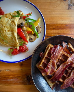 Breakfast table with bacon waffles in a skillet and a vegetable omelette on a plate on a wooden surface