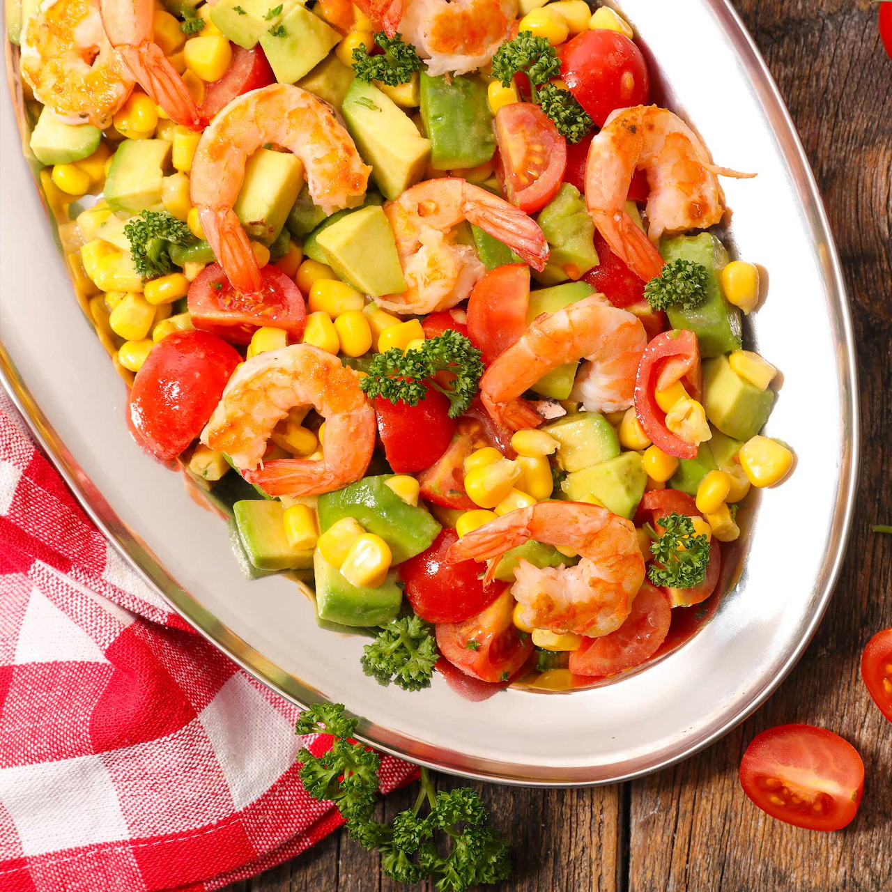 Colorful shrimp and vegetable stir fry in white oval dish with red checkered napkin