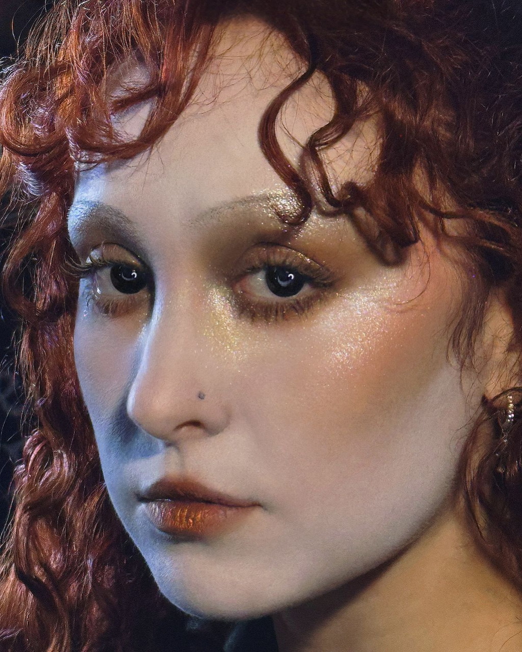Close-up portrait of a woman with curly red hair, smoky eye makeup, and orange-red lips