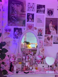 Pink vanity desk with mirror, beauty products, and coquette wall collage illuminated by purple LED lights