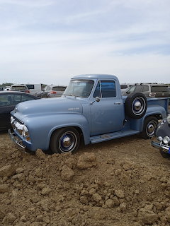Vintage 1950s light blue Ford pickup truck parked on dirt at an outdoor car show