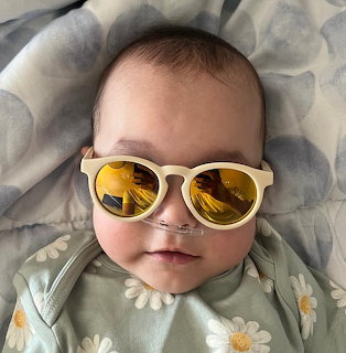 Baby lying on a blanket wearing white sunglasses with yellow reflective lenses