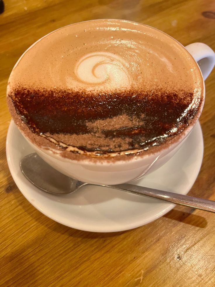 Cappuccino with latte art foam in white cup on saucer with spoon