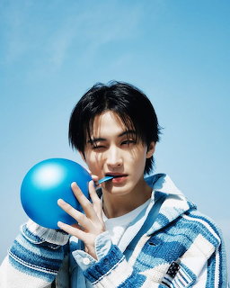 Young man with dark hair holding a blue balloon near his face wearing a blue and white striped hoodie